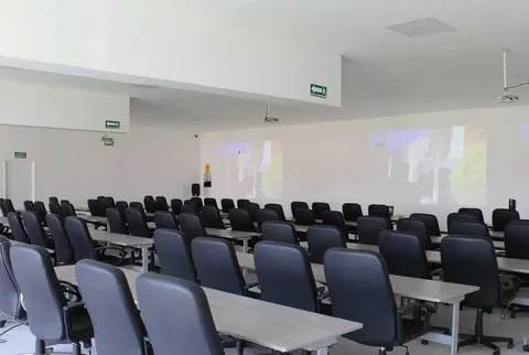 Salón amplio con filas de mesas, sillas ejecutivas y proyección al frente